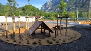 Aire de jeux nature avec cabane en bois et copeaux au pied des montagnes, aménagement paysager en cours.